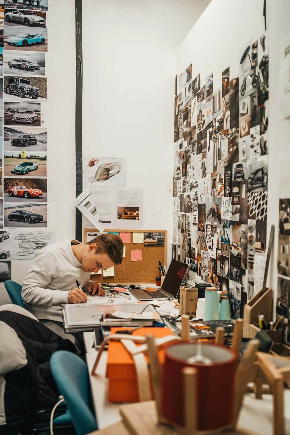 Product designer sketching car designs at a busy studio desk.