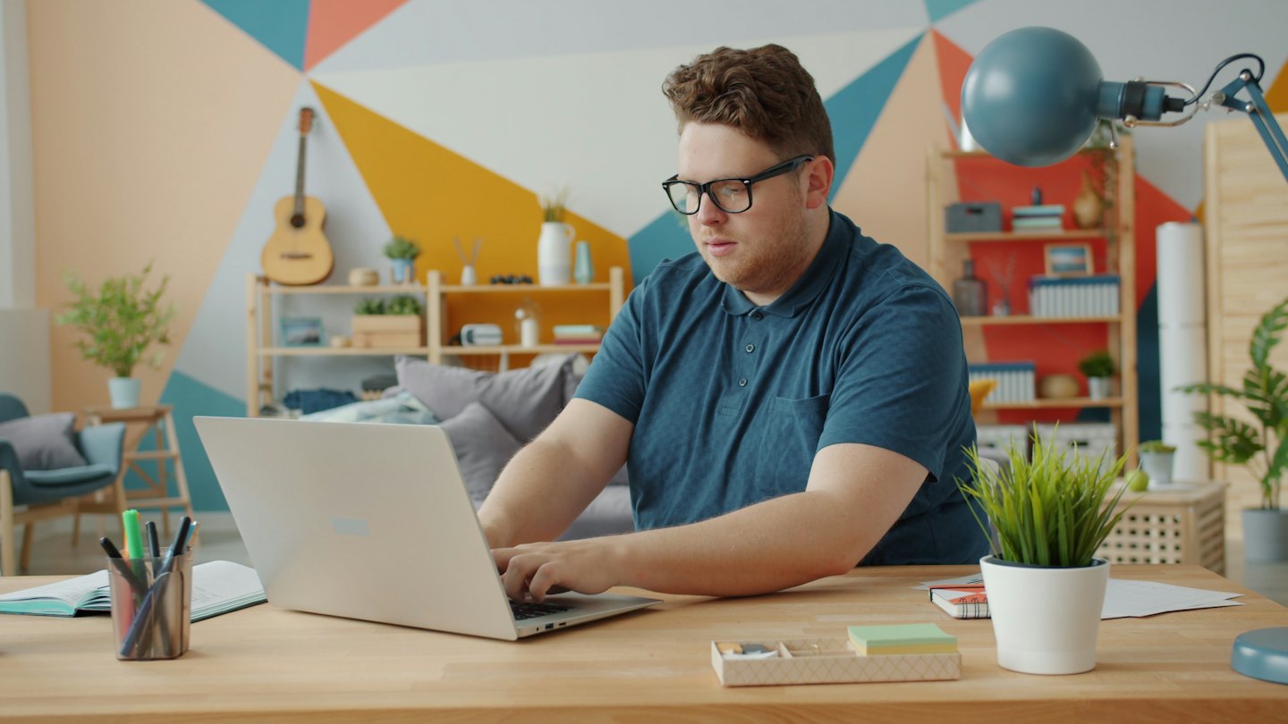 Man wearing glasses types on a laptop at a desk.